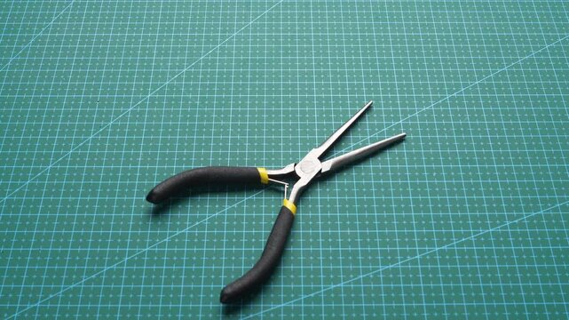 Hand placing precision needle-nose pliers on green cutting mat for electronics repair or crafting