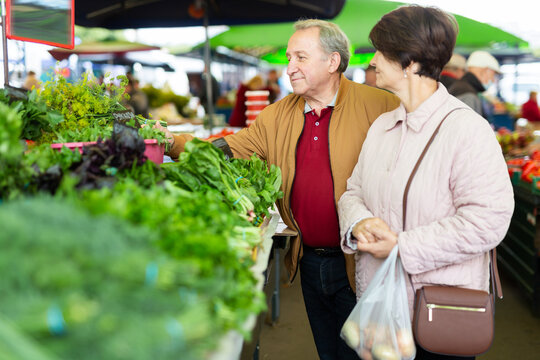 elderly man and woman buy greens at an open market