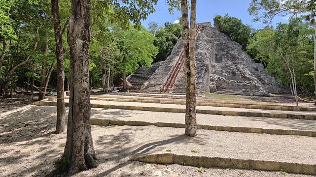 Ancient Mayan stone temple surrounded by lush tropical jungle at the Coba archaeological site in Quintana Roo, Mexico. Historic pyramid rising above archaeological ruins under a bright blue sky, showc