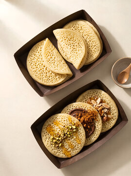 Top view of delicious Moroccan msemen pancakes served in cardboard trays with sweet toppings, presented artfully on a neutral background