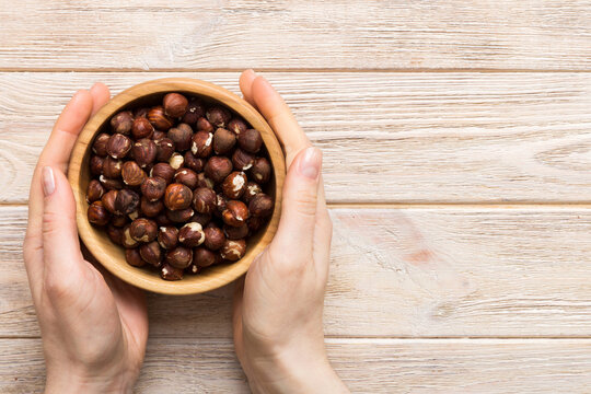Woman hands holding a wooden bowl with hazelnut nuts. Healthy food and snack. Vegetarian snacks of different nuts
