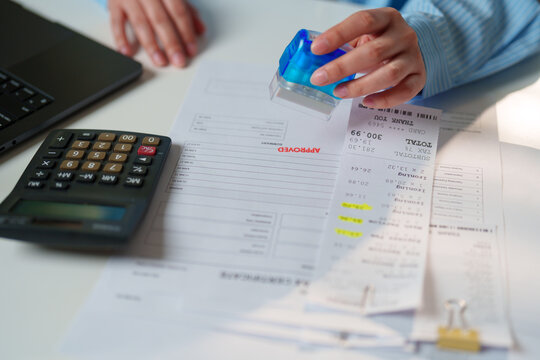 Close-up of a professional approving financial documents with a stamp, calculator, receipts, and invoices, accounting workflow, financial control, business approval, and expense verification