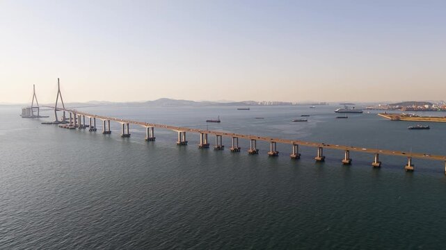 Incheon Bridge spanning calm bay with traffic crossing above cruise ship and cargo vessels anchored near shore