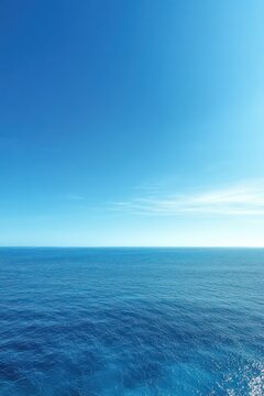 Calm open ocean and clear blue sky meeting at a distant horizon with sunlight shimmering on the water, serene and expansive