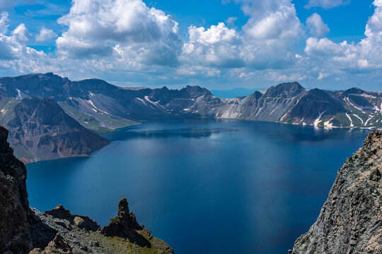 Panoramic view of Heaven Lake surrounded by rocky peaks under blue sky at Mount Paektu
