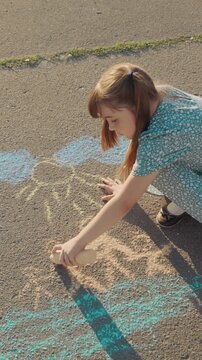Girl is drawing on the sidewalk with chalk. She is wearing a blue dress