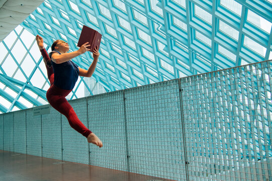 A dancer leaps holding a book 