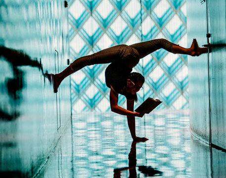 A woman performs a handstand reading a book in a library 