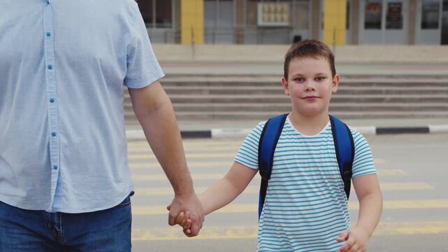 Schoolboy on the way to class, Parent support on school day, Safe walk to school, Cheerful boy ready to learn, Smiling child with backpack, Steps of childhood journey, Holding hands with dad