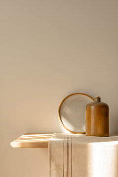 Wooden shelf with linen napkin, clay pottery kitchenware, bottle and plate, neutral beige empty wall background with natural sunlight shadows, aesthetic sustainable home interior, cottage core