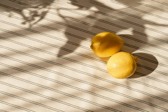 two lemons on striped beige linen tablecloth with natural abstract sunlight shadows, aesthetic summer lifestyle background with copy space