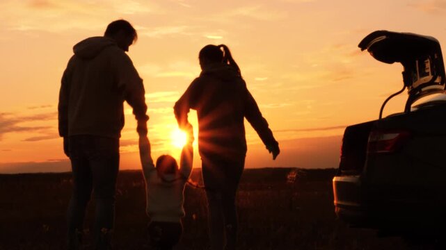 Silhouettes of having fun mom dad kid. Golden sunset, cheerful joyful family at holidays holding hands, lifting baby girl high in air, playing together. Fun active game. Traveling by car to nature.