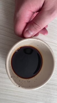 Top View of Man's Hand Taking a Ceramic Cup of Fresh Black Coffee from a Wooden Table