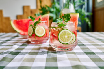 Obraz premium Summer refreshing watermelon drink with ice, mint and slices of lime on the table. Fresh healthy cold melon beverage. Fruit infused water, herbs and lemon.