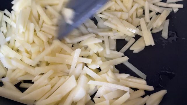 Close-Up Shot of Stirring Raw Sliced Potatoes in Pan with Spatula During Home Cooking