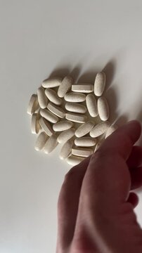 Top View of Hand Adjusting and Sweeping Away Vitamin Pills on White Background