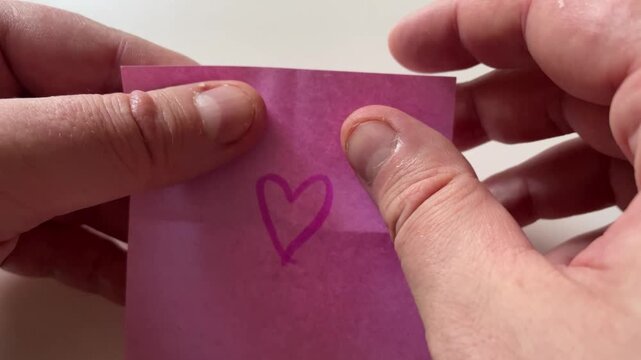 Person Tearing Pink Note Paper with Drawn Heart Symbol in Half Concept of Heartbreak and Separation. Close-Up