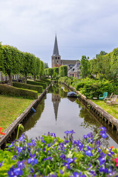 Quiet canal with historic church tower and trimmed trees in IJlst, Friesland, Netherlands