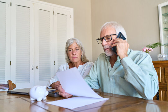 Retirement Planning And Financial Protection: Senior Couple Manages Finances, Reviews Documents, And Seeks Professional Advice On Phone