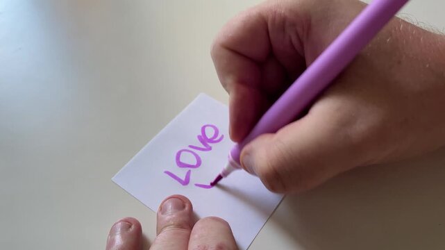 Hand Writing "Love You!" with Pink Marker on Small White Note - Romantic Message Concept. Close-Up