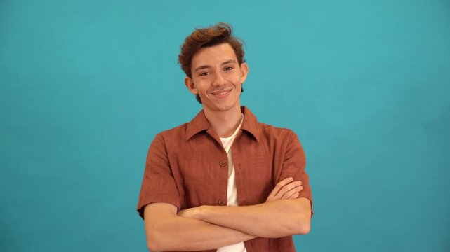 Confident young man smiling with arms crossed on a blue background