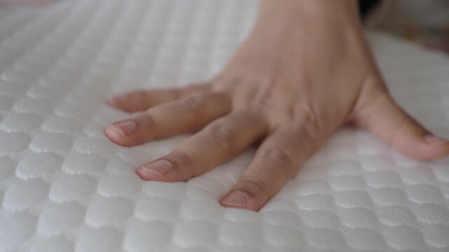 Close up slow motion video of hand pressing on soft white mattress or pillow, testing the comfortable and elastic material of bedding