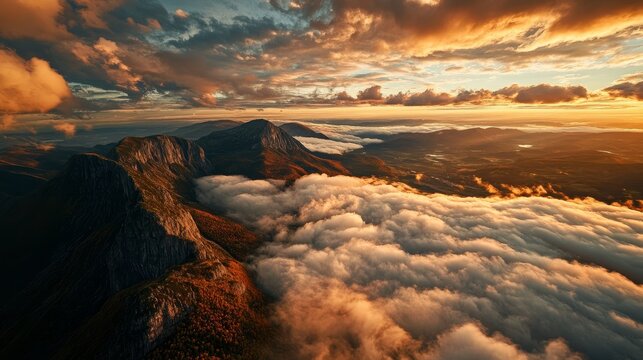 Panoramic aerial view of rugged mountains emerging from a sea of clouds at sunset with sky