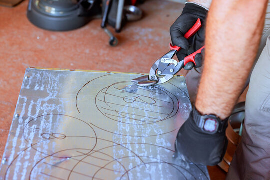 Worker is using tin snips to cut metal sheet during HVAC duct assemble tools workspace are visible.