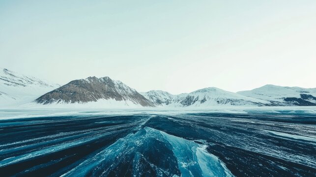 Panoramic view of a vast frozen ice field with snow-covered mountains under a clear sky
