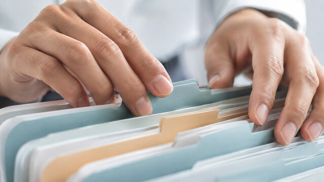 "Close‑up of two hands sorting file folders with colored tabs in an office setting, symbolizing organization, administrative work, and efficient data management with professional clarity and precision
