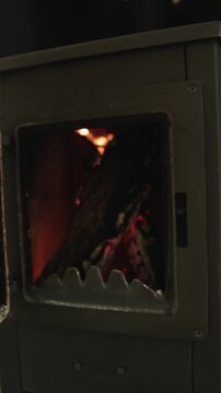 Vertical video. First-person view of a hand opening a wood stove with burning firewood inside.