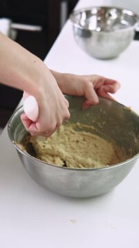 Vertical video. Bakery occupation. Kneading dough. Confectioner female hand stirring flour mass in metal bowl with kitchen spatula.