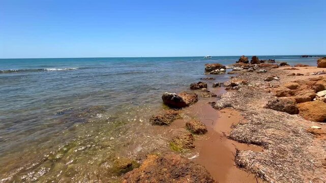 Rocky Mediterranean beach on the coast of Sicily with crystal clear water, gentle sea waves and sunny summer weather. Peaceful coastal landscape with natural rocks and turquoise sea.