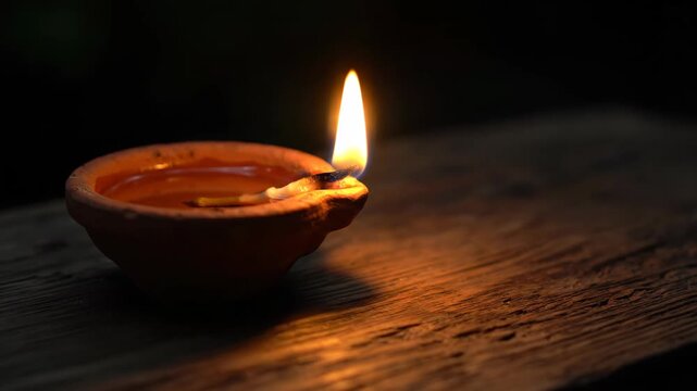 Lit clay diya lamp burning on wooden surface at night