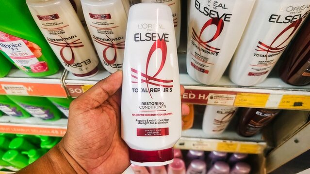 Malaysia Kuala Terengganu, 21 July 2026: A hand holding a L'Oreal Paris Total Repair 5 Repairing Shampoo bottle for damaged hair, featuring Keratin-XS, held by a hand in a supermarket