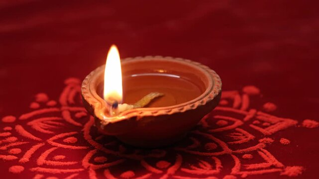 Lit clay diya lamp on red rangoli for Diwali festival