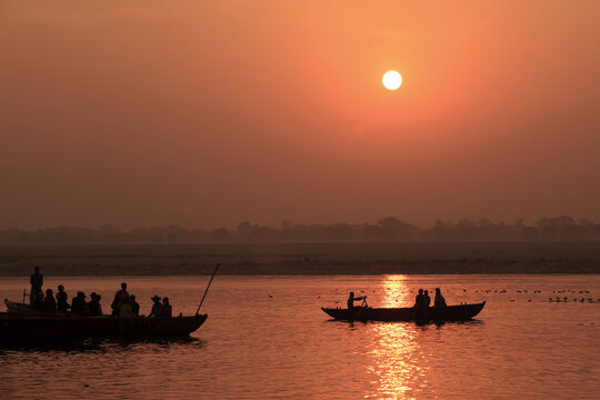 Silhouettes of passengers aboard wooden boats at sunrise on the Ganges River in Varanasi, India