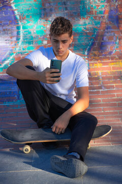 Boy looking at cell phone sitting on his skateboard