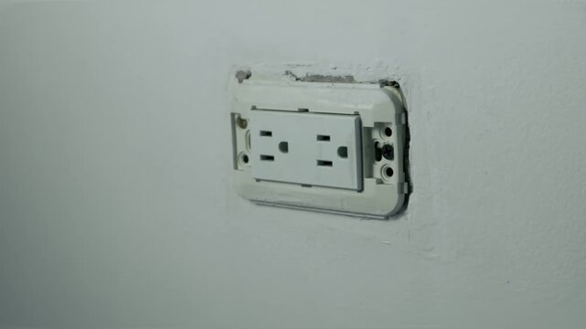 Close-up of uncovered electrical wall outlet with missing faceplate mounted on white interior wall, 4K 60fps video