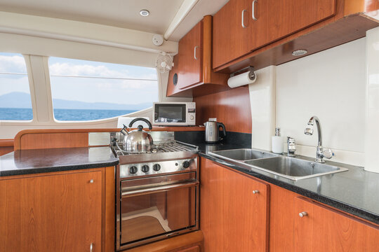 Clean and modern galley kitchen of a charter private sailing catamaran with wooden cupboards, sink, oven, microwave and kettle, with Mediterranean sea view, in a marina