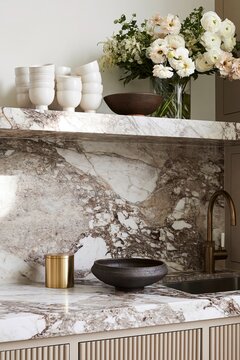 Kitchen shelving area featuring Calacatta Viola marble with white porcelain cups, dark stoneware bowl, and brushed brass canister in a modern design