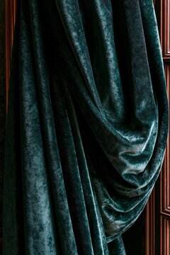 Closeup of emerald green velvet curtain fabric with soft window light highlighting the texture and deep folds of the luxurious drape