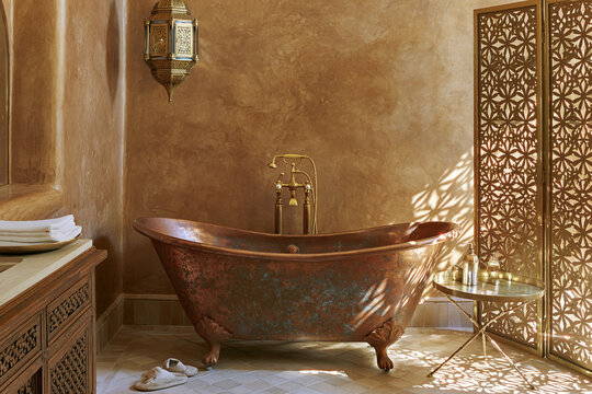 Freestanding copper clawfoot tub with aged patina in a warm ochre lime-washed bathroom illuminated by dappled afternoon light