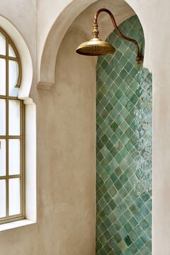 Shower alcove in Moroccan riad bathroom featuring emerald zellige tiles and aged brass rainfall showerhead with patinated copper arm