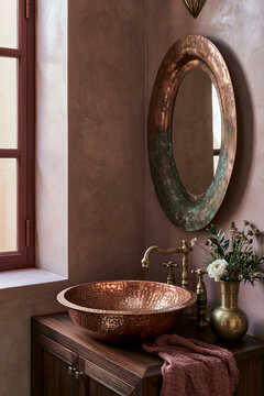 Moroccan-inspired bathroom vanity corner featuring a hand-hammered copper sink, patinated brass fixtures, and a textured rose-toned wall