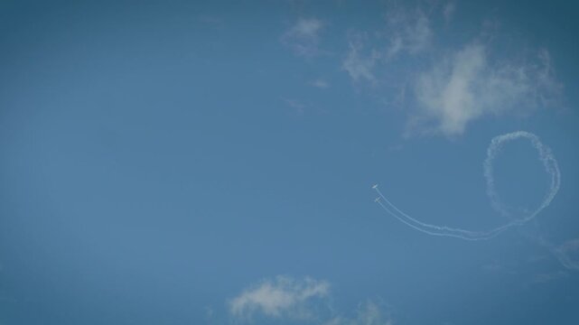A white smoke loop pattern created by an aerobatic airplane in a clear blue sky with soft white clouds.