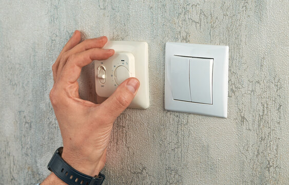 Hand adjusting a home thermostat on the wall to control room temperature. Close-up of heating regulation, energy efficiency, climate control, and smart home comfort