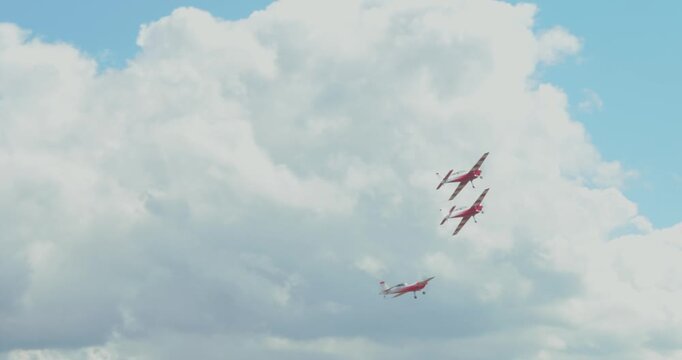 Red small propeller airplanes flying in blue cloudy sky near airport windsock