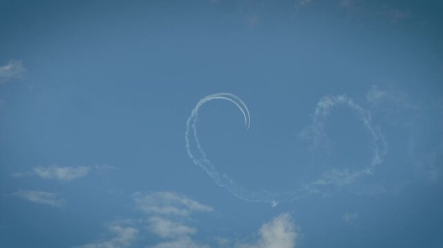 Precision aerobatic aircraft complete a perfect loop with contrails over white clouds.
