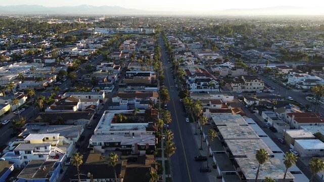 Suburban street network displays premium residential housing in Huntington Beach, California. Palm trees line asphalt roads intersecting through established upscale neighborhoods, flat roof condos